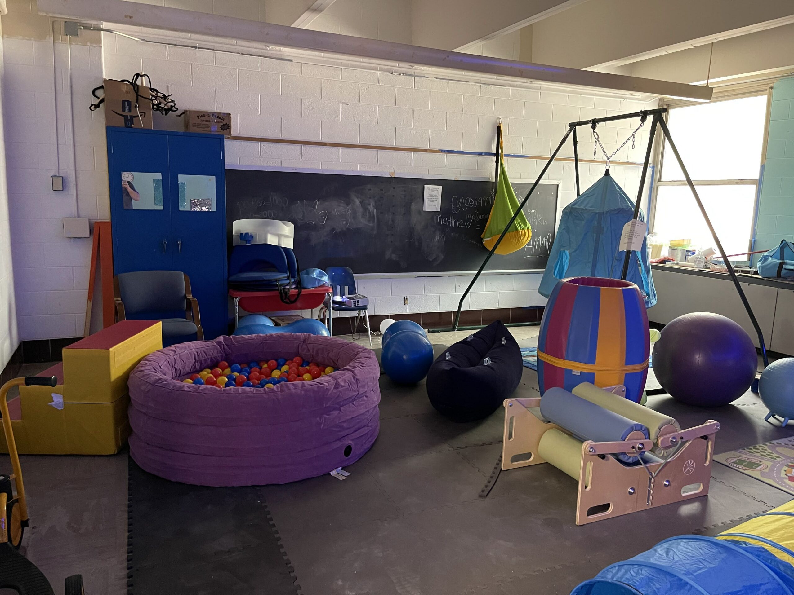 A picture of the sensory room featuring a ball pit, swing set, and squeeze machine.